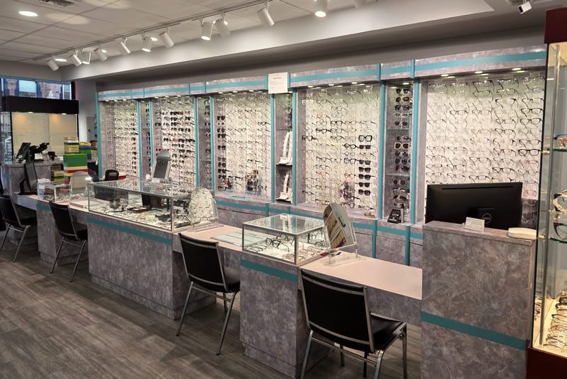 The dispensary, with hundreds of eyeglass frames on backlit wall displays above grey marble counters and glass display cases.