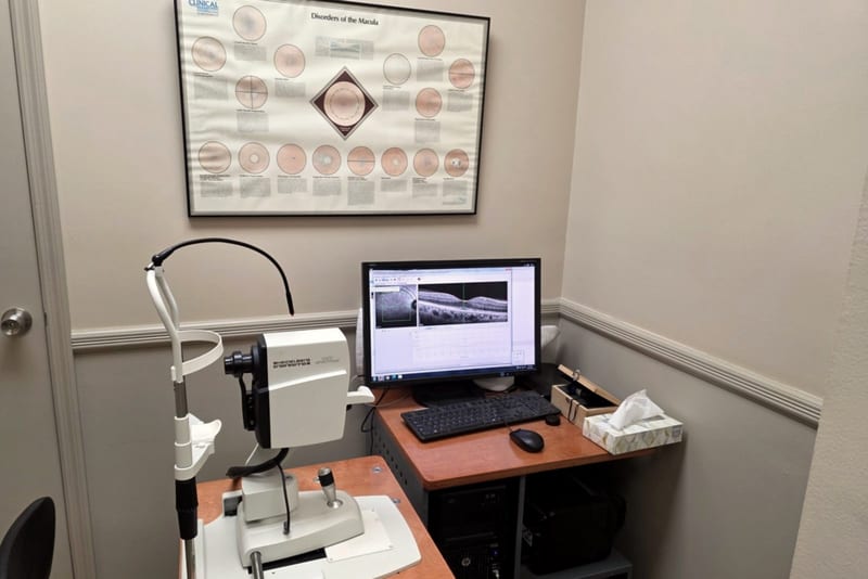 A Heidelberg SPECTRALIS OCT scanner beside a monitor showing a cross-sectional scan of the retina, below a framed reference chart of macular disorders.