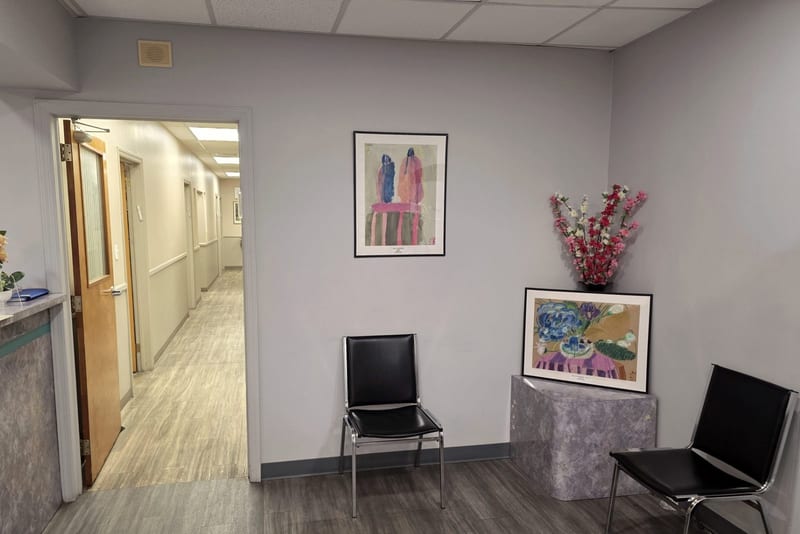 A second seating area with two chairs and framed paintings, beside the corridor leading to the examination rooms.